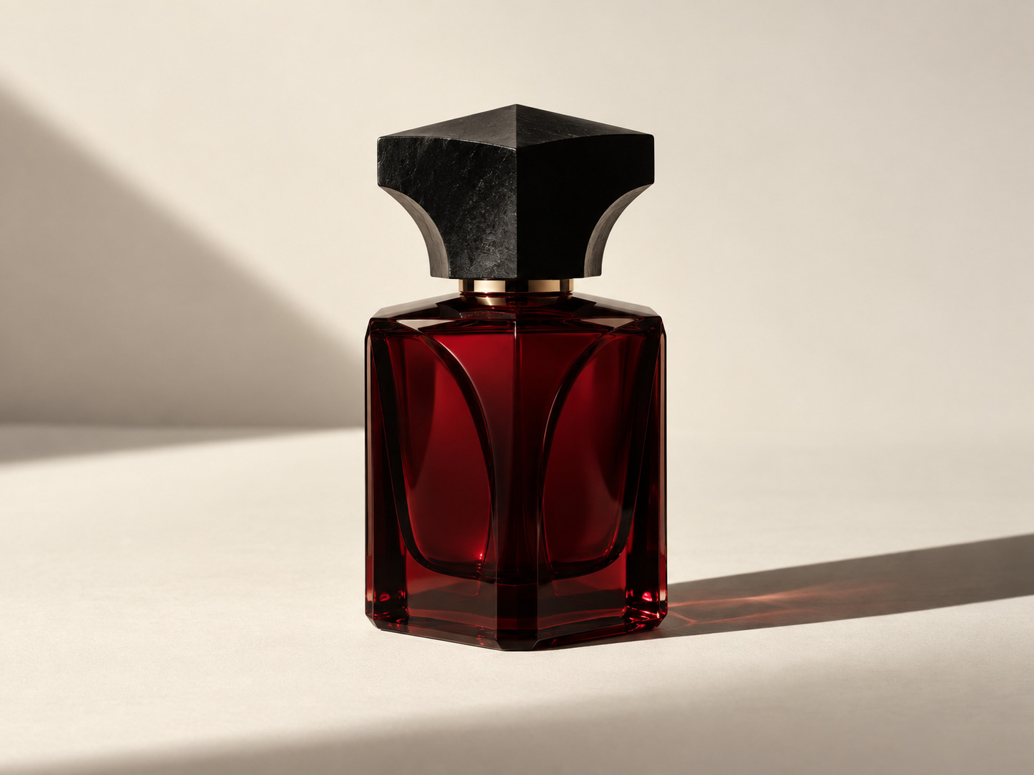 A sculptural oxblood glass perfume bottle in directional light